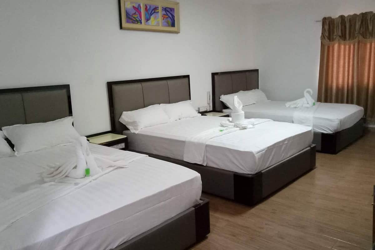 A hotel room with three beds, each with white linens and pillows, a bedside table with a lamp, and a painting on the wall.