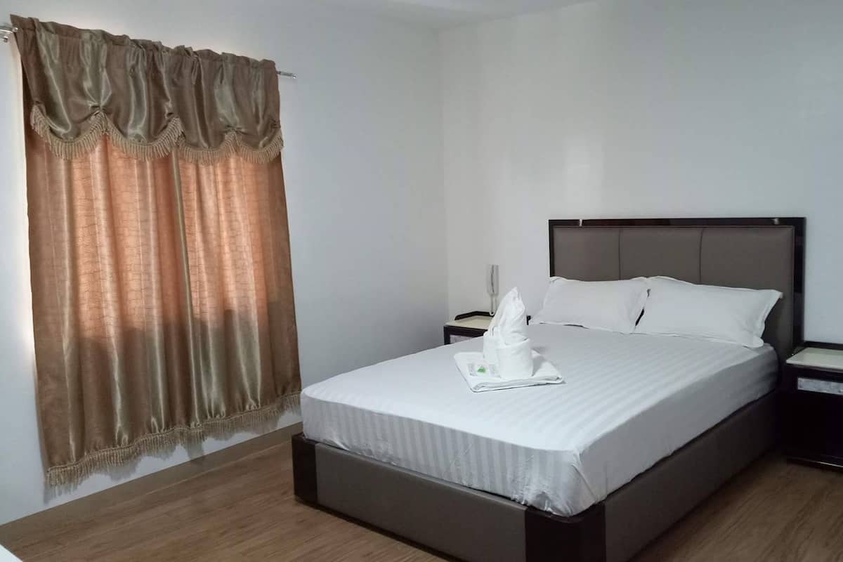 A hotel room with a bed, a nightstand, and a window with curtains.
