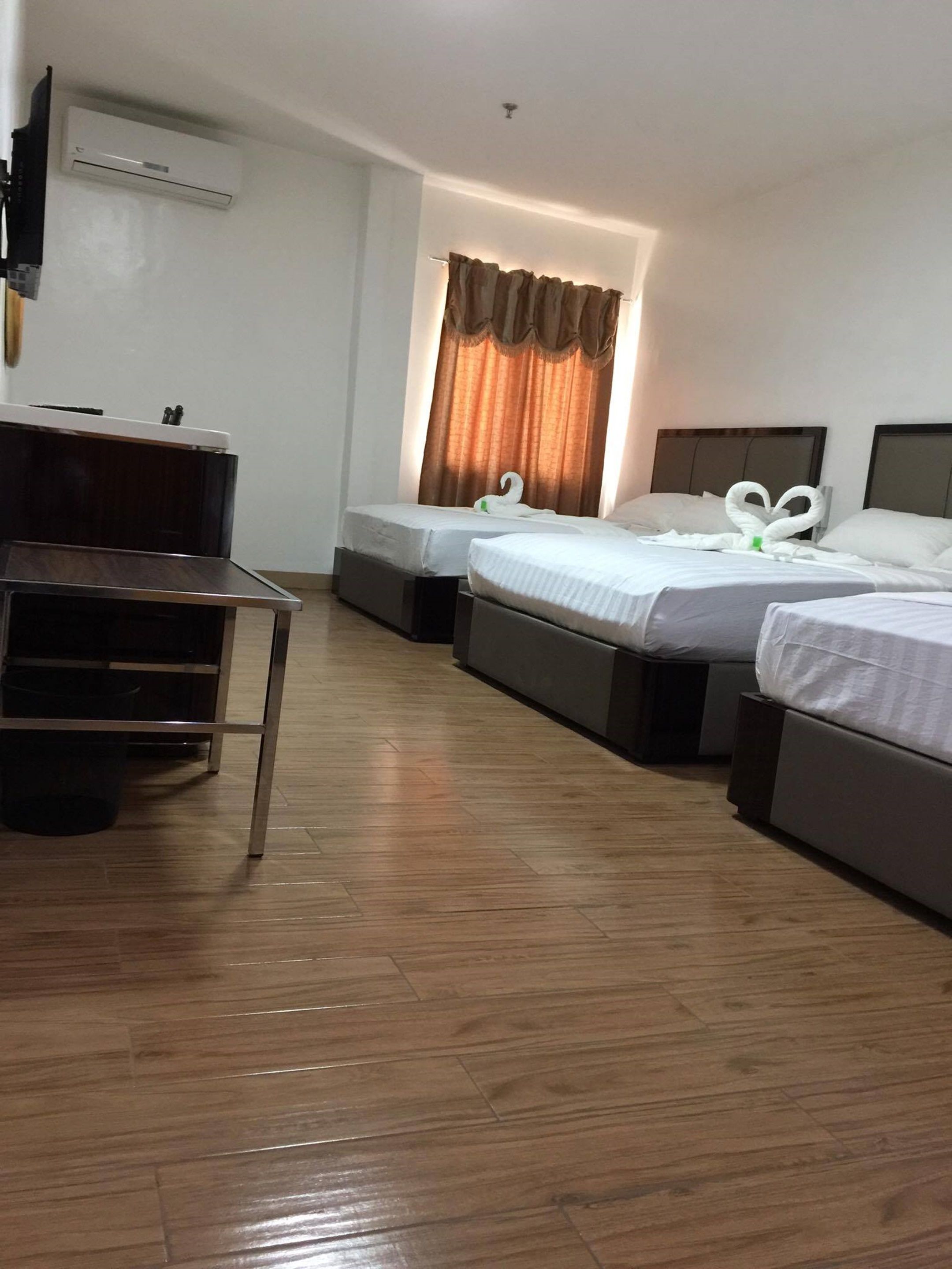 Hotellihuoneessa on kaksi erillistä sänkyä, työpöytä ja tuoli. Seinällä on ilmastointilaite ja ikkunassa on verhot.