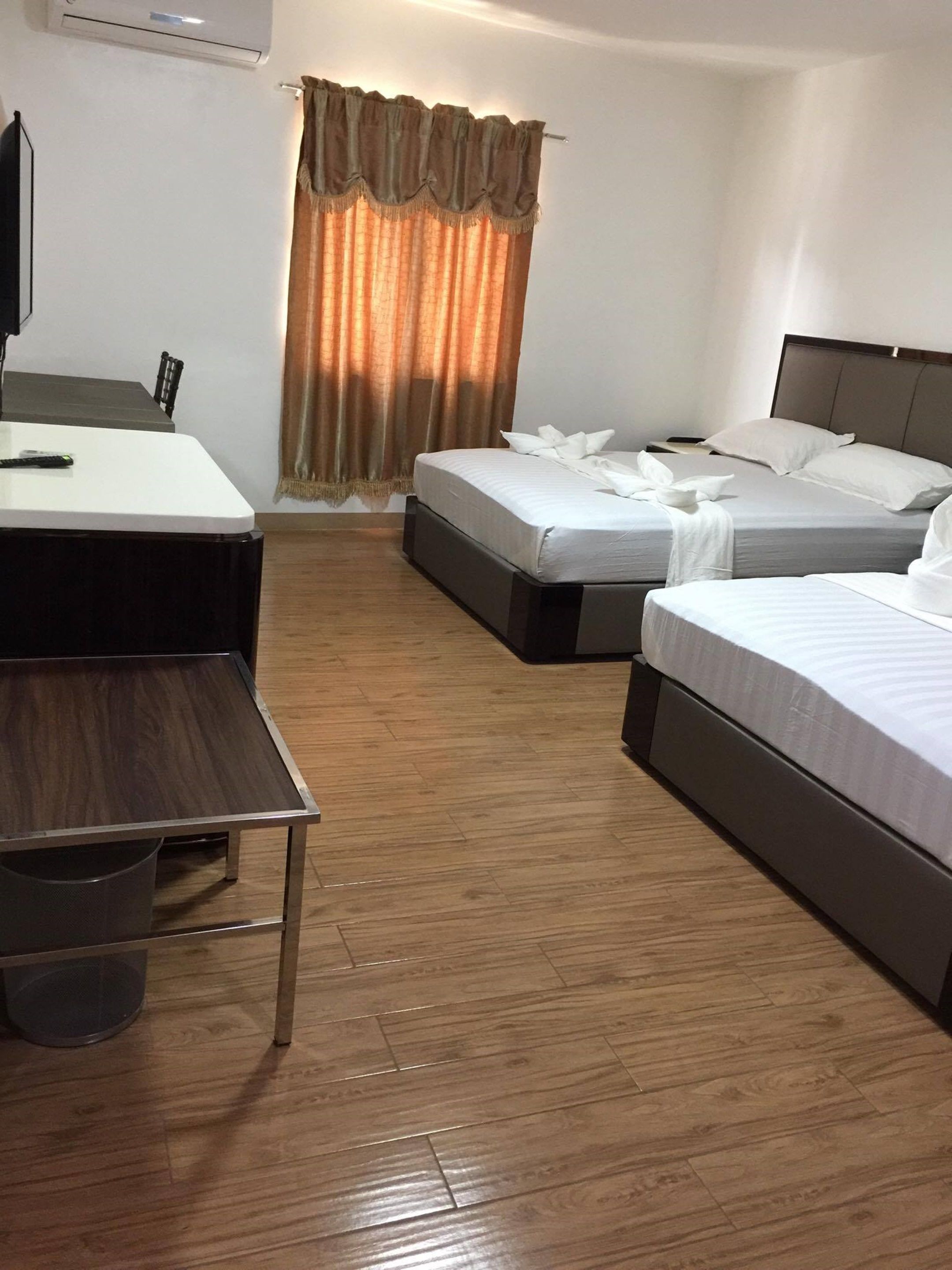 A hotel room with two single beds, a desk, a chair, and a television.