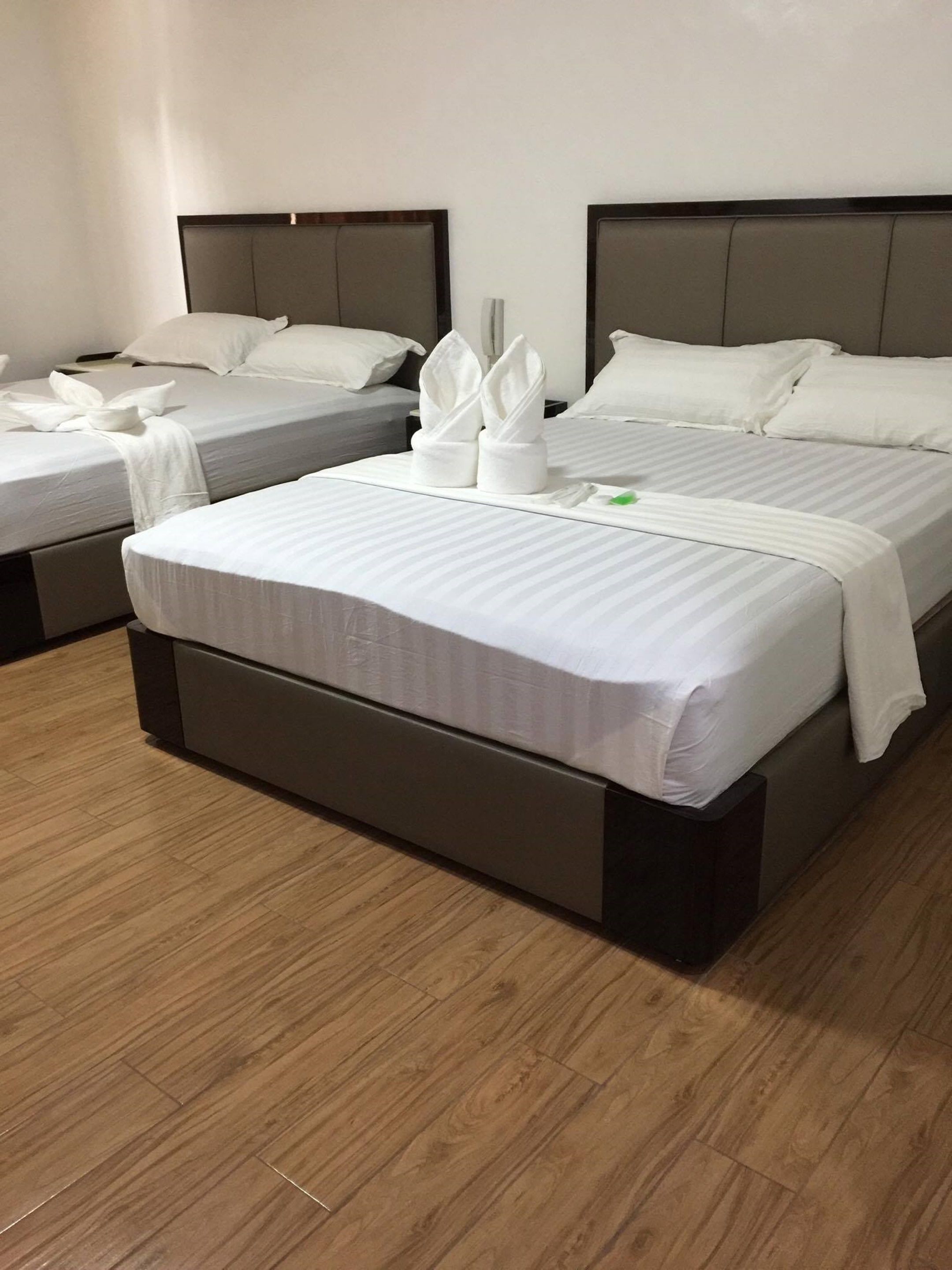 A hotel room with two beds, each with white linens and pillows, and a wooden floor.