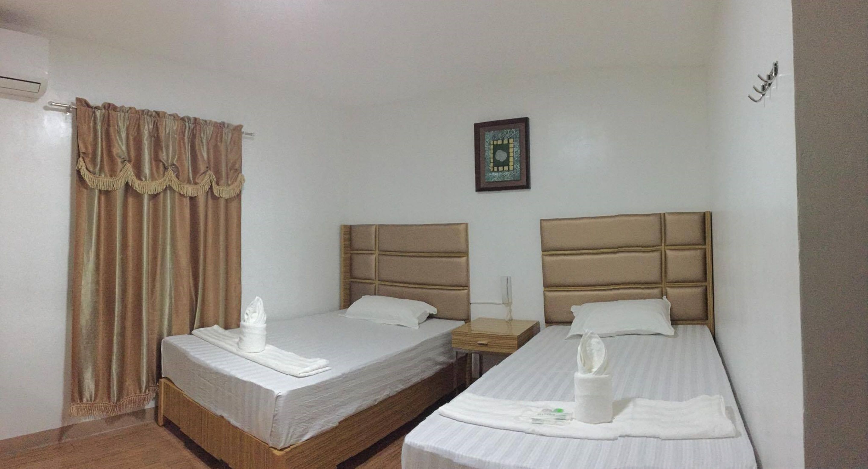 A hotel room with two beds, a nightstand, a framed picture on the wall, and a window with curtains.