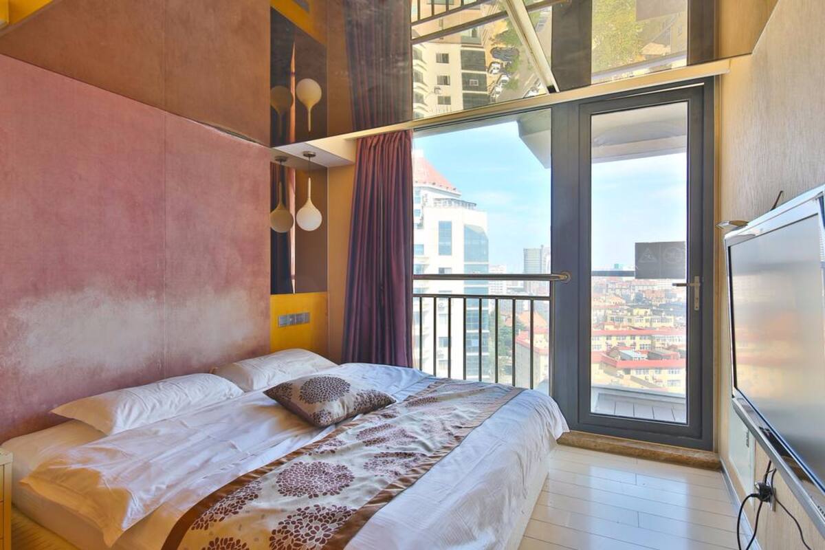 Un dormitorio moderno con una cama grande, un balcón con vista a la ciudad y un ventanal amplio.