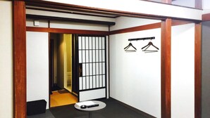 A small, modern room with a wooden-framed sliding door, a small round table with a remote control, and two hangers on the wall. - Tennoji Lagoon Hotel (Osaka)