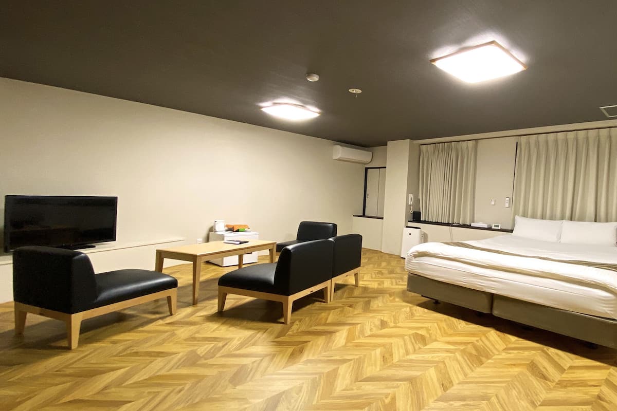 Ein Hotelzimmer mit Bett, Fernseher, Schreibtisch, zwei Stühlen und einem Holzboden mit Fischgrätmuster.
