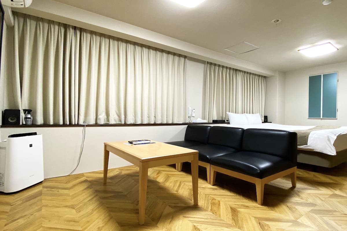 Ein Hotelzimmer mit einem Bett, einer Couch, einem Tisch, einem Fernseher und einem Fenster mit Vorhängen.