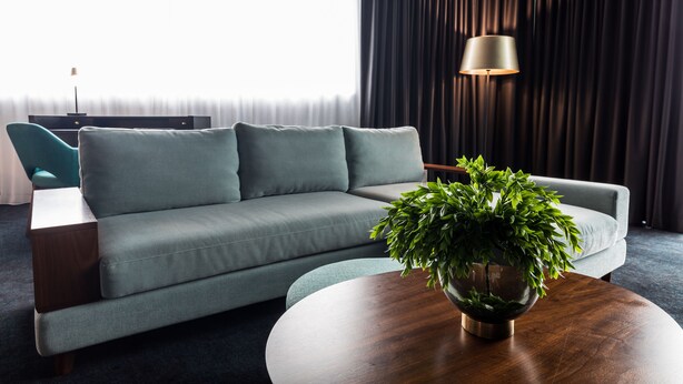 Una sala de estar moderna con un sofá gris, una mesa de centro redonda de madera y una planta verde, junto con una lámpara de pie.