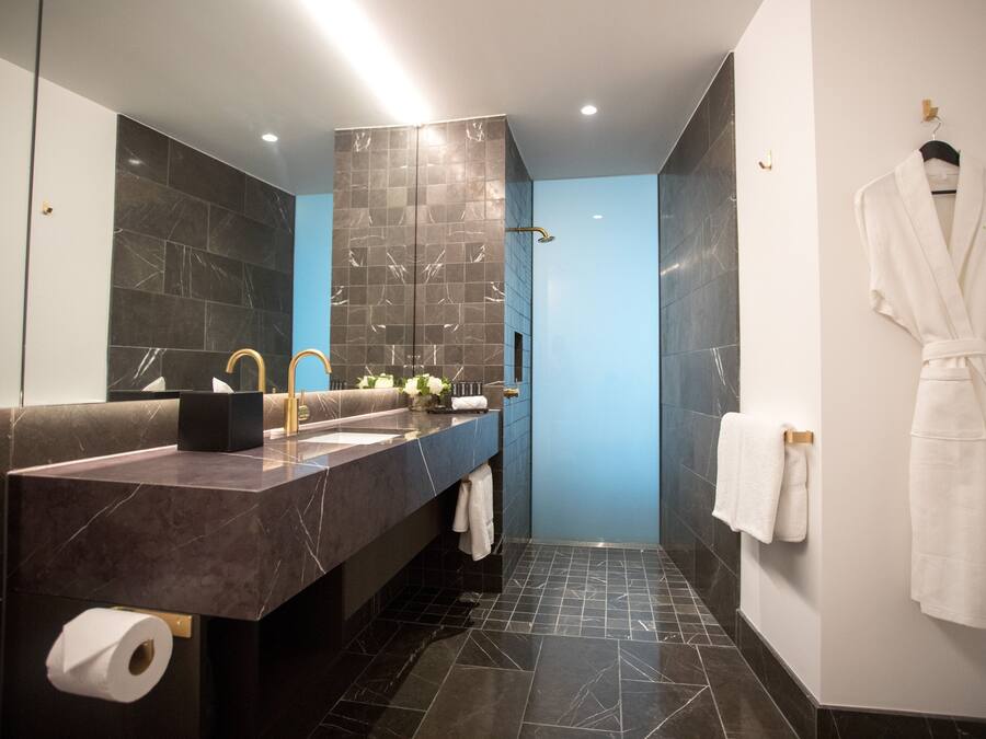 Un baño moderno con tocador de mármol, un espejo grande, zona de ducha y una bata colgada en la pared.