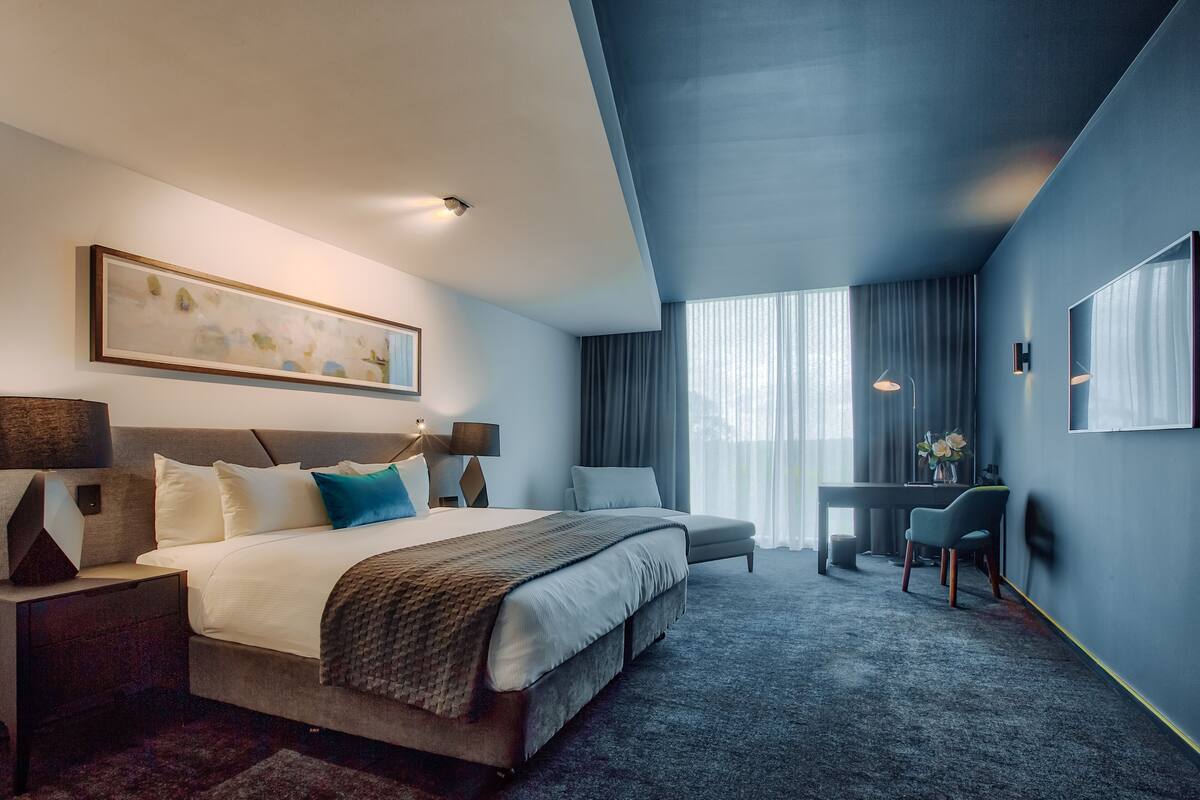 A modern hotel room with a large bed, bedside tables, a desk, and a chair.