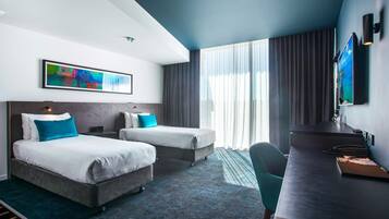 A modern hotel room with two beds, a desk, and a large window with curtains.