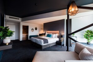 Una habitación de hotel moderna con una cama grande, mesitas de noche, un escritorio y vistas al exterior.