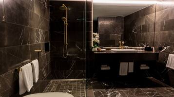 Ein modernes Badezimmer mit dunklen Marmorwänden, einer Glastrennwand zur Dusche, einer weißen Badewanne und einem Waschtisch mit Spüle und Handtuchhalter.