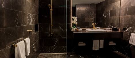 A modern bathroom with dark marble walls, a glass-enclosed shower, a white bathtub, and a vanity with a sink and towel rack.