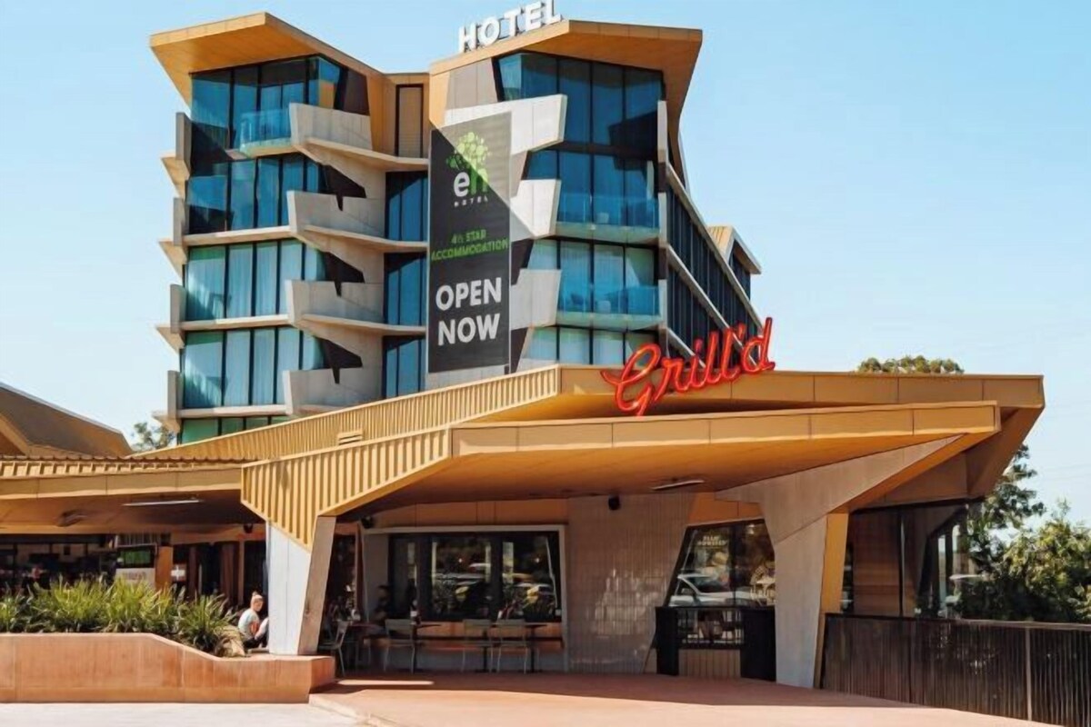 A modern hotel with a prominent 'OPEN NOW' sign, a rooftop terrace, and a 'GRAND' sign indicating a grand hotel.