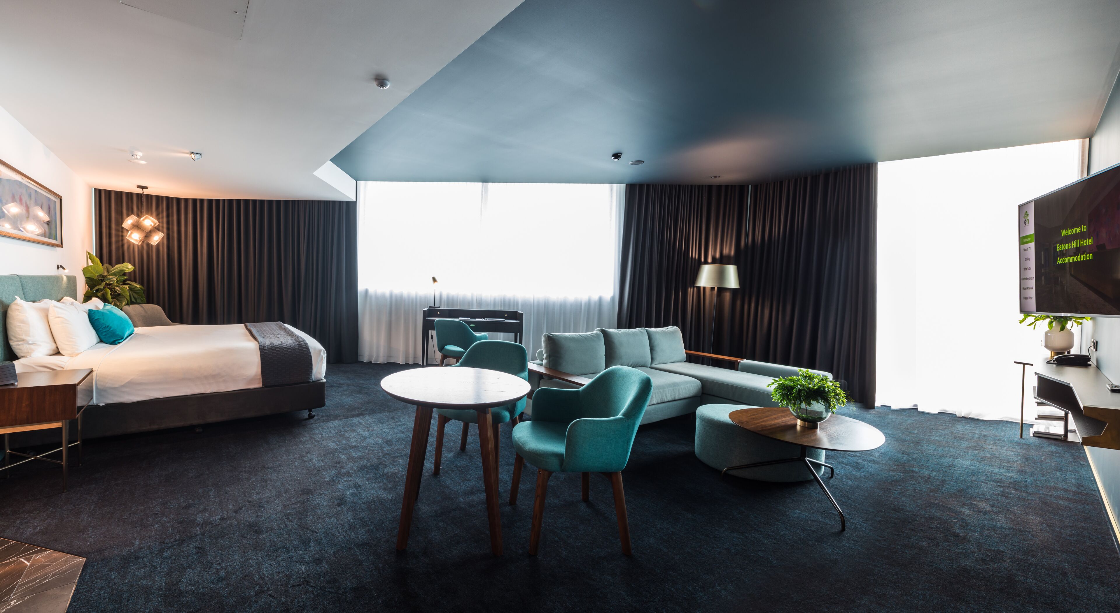 Et moderne hotelværelse med seng, sofa, stole, et lille bord og et fjernsyn.