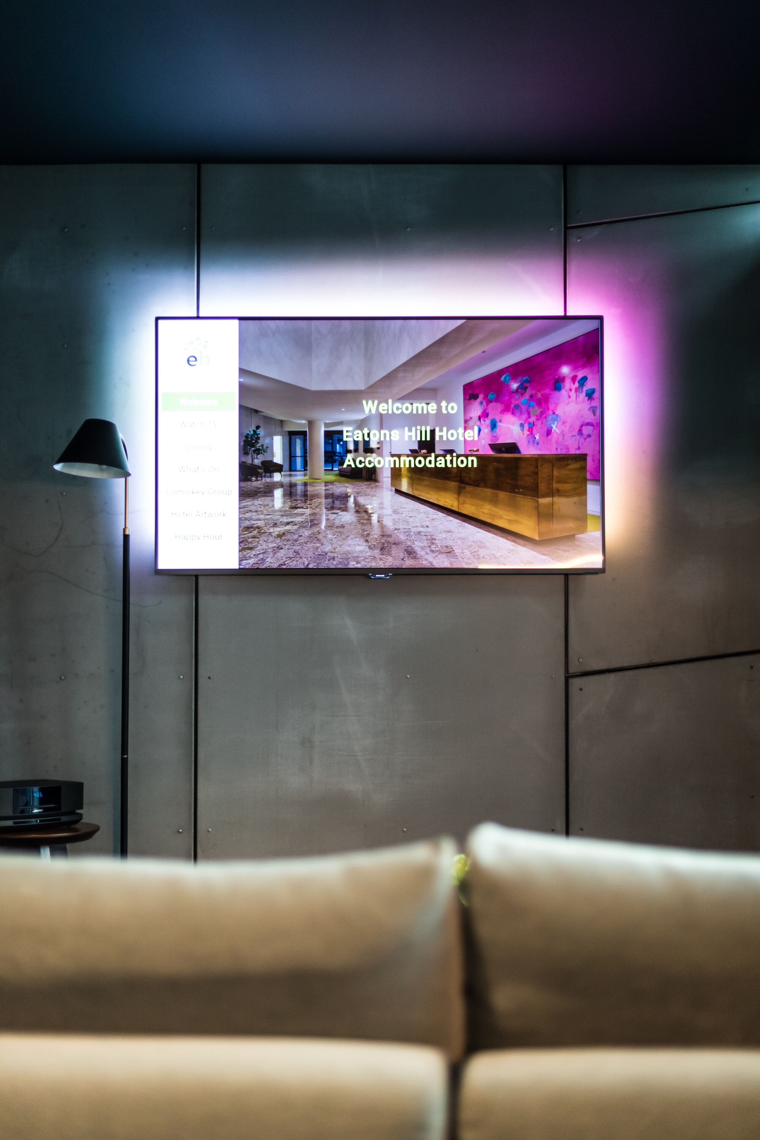 Un televisor muestra la pantalla de bienvenida del hotel, con un mostrador de recepción y un interior moderno.