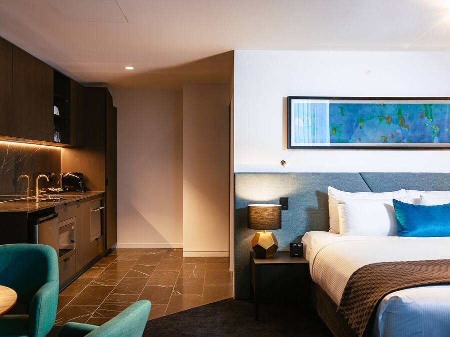A hotel room with a bed, bedside table, lamp, and a painting on the wall.