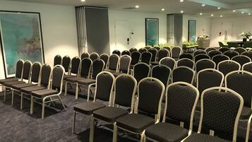 A conference room with rows of chairs and tables, a projector, and a large abstract painting on the wall.