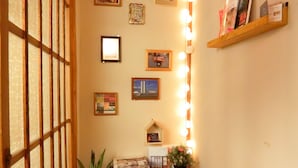 Un couloir avec une porte en bois, une plante en pot et une étagère contenant des livres, dont un petit livre rouge.