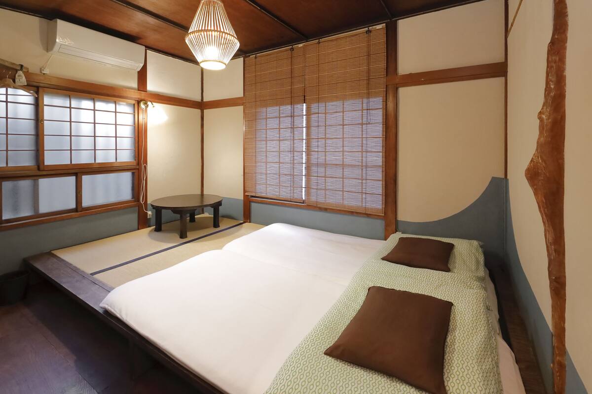 Ein traditioneller japanischer Raum mit Tatami-Böden, einer niedrigen Plattformliege, einem kleinen runden Tisch und Shoji-Schirmen.