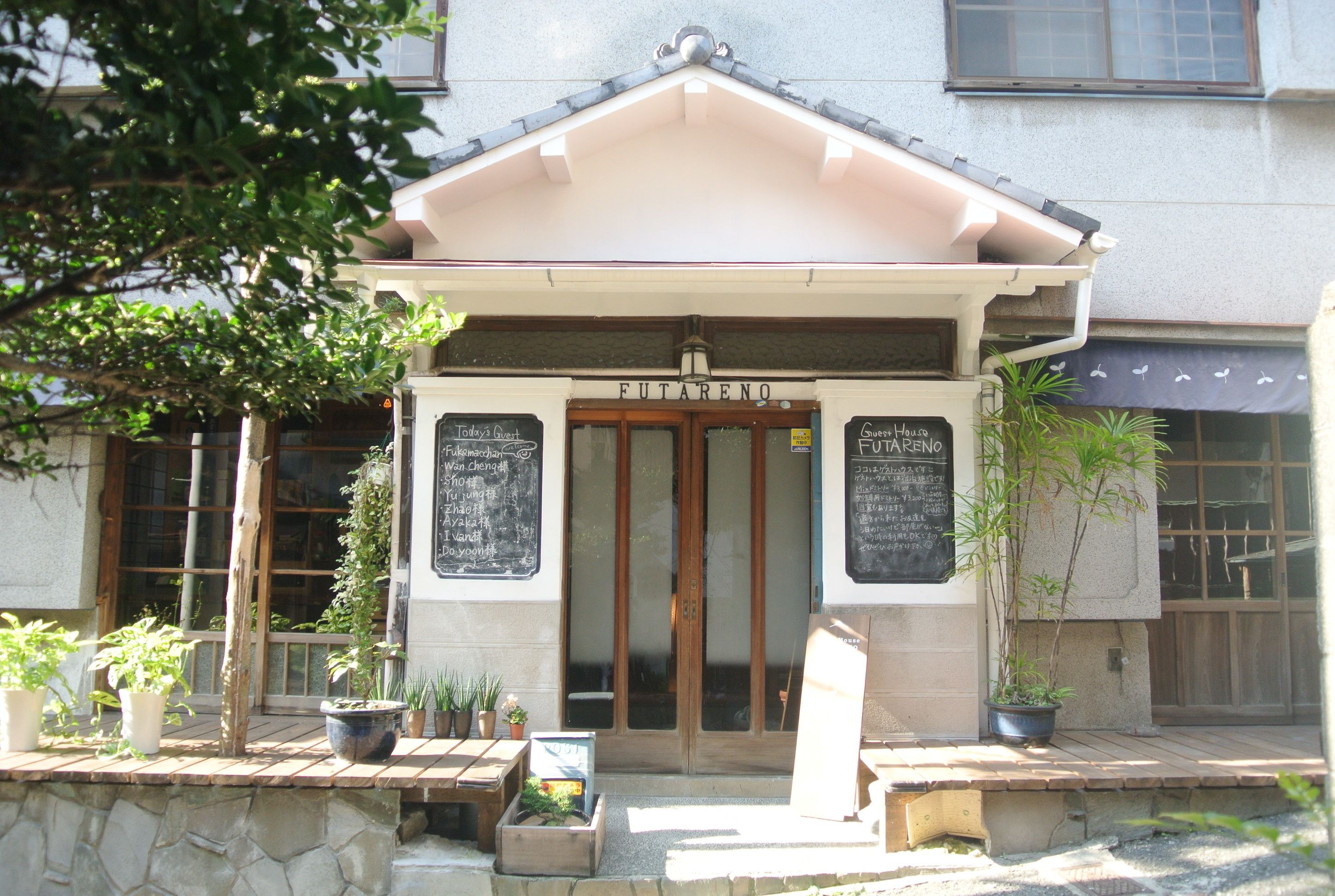 A building with a sign reading "Futareno" and a wooden door. There are potted plants on the ground and a stone wall in front.