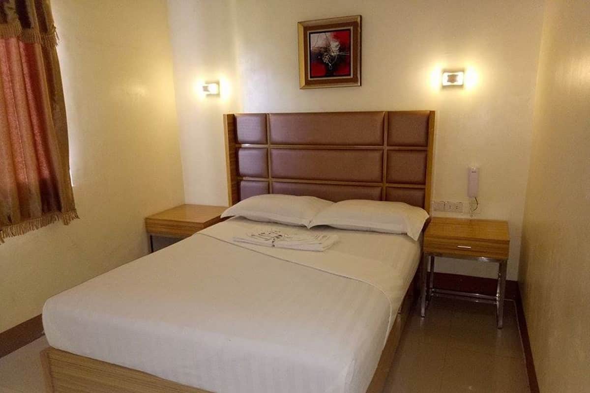 Una cama bien hecha con cabecera, dos mesitas de noche y una lámpara de pared.