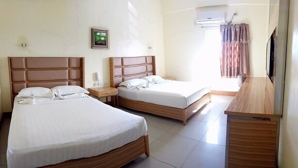 Una habitación de hotel con dos camas, un aparador de madera, una mesita de noche con lámpara y aire acondicionado instalado en la pared.