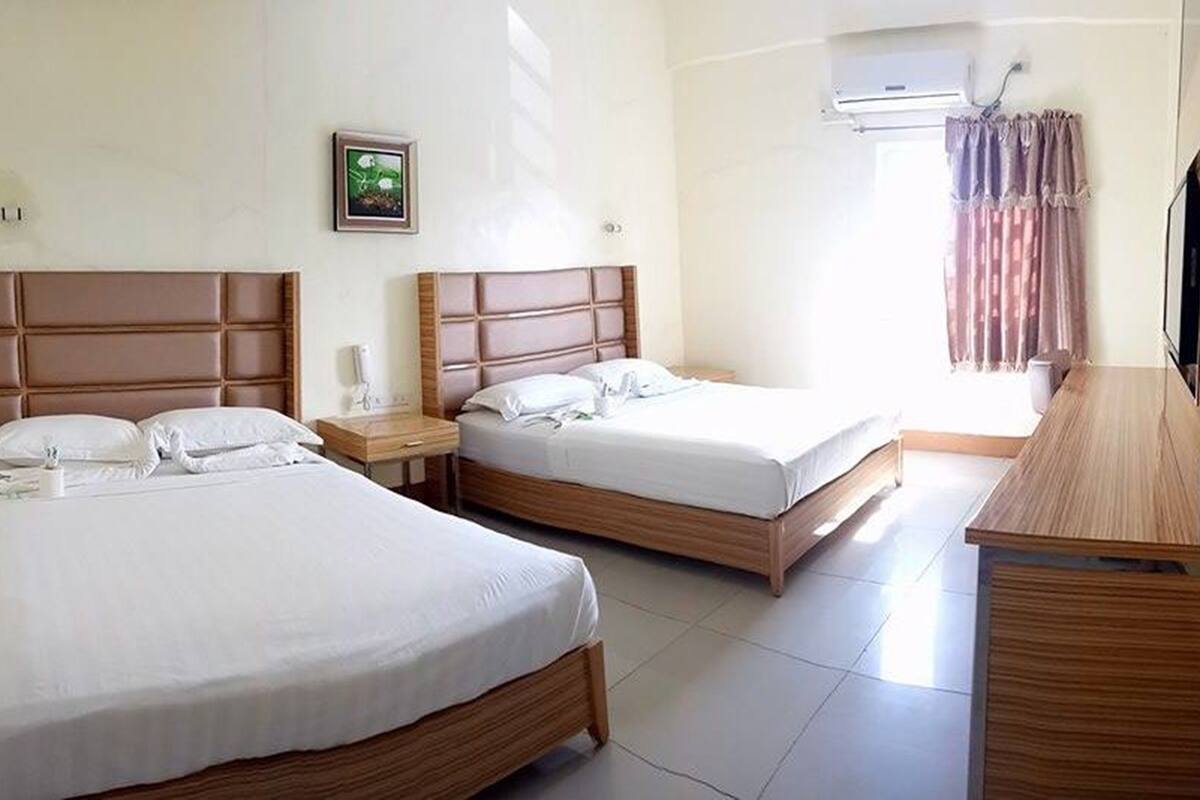 Una habitación de hotel con dos camas, un aparador de madera, una mesita de noche con lámpara y aire acondicionado instalado en la pared.