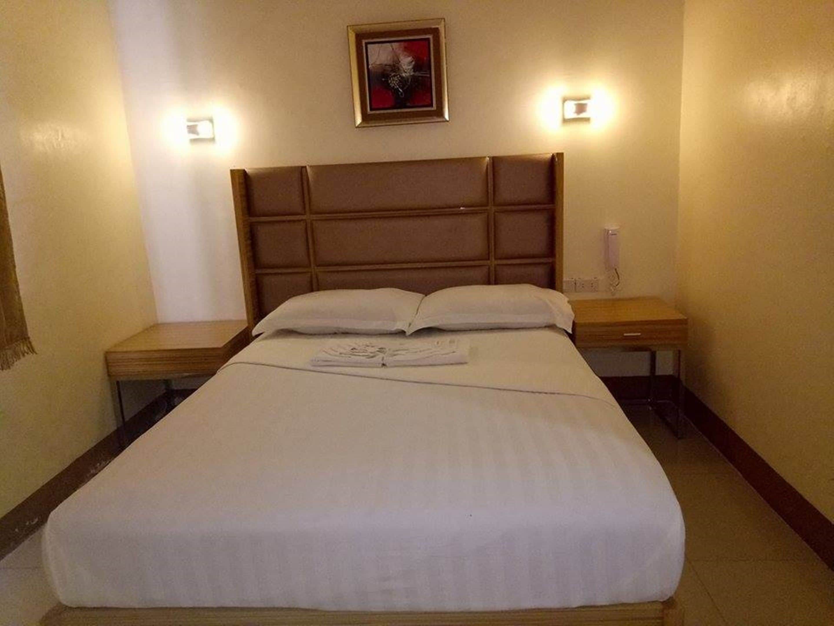 Quarto de hotel com uma cama grande, duas mesas de cabeceira e uma cabeceira.