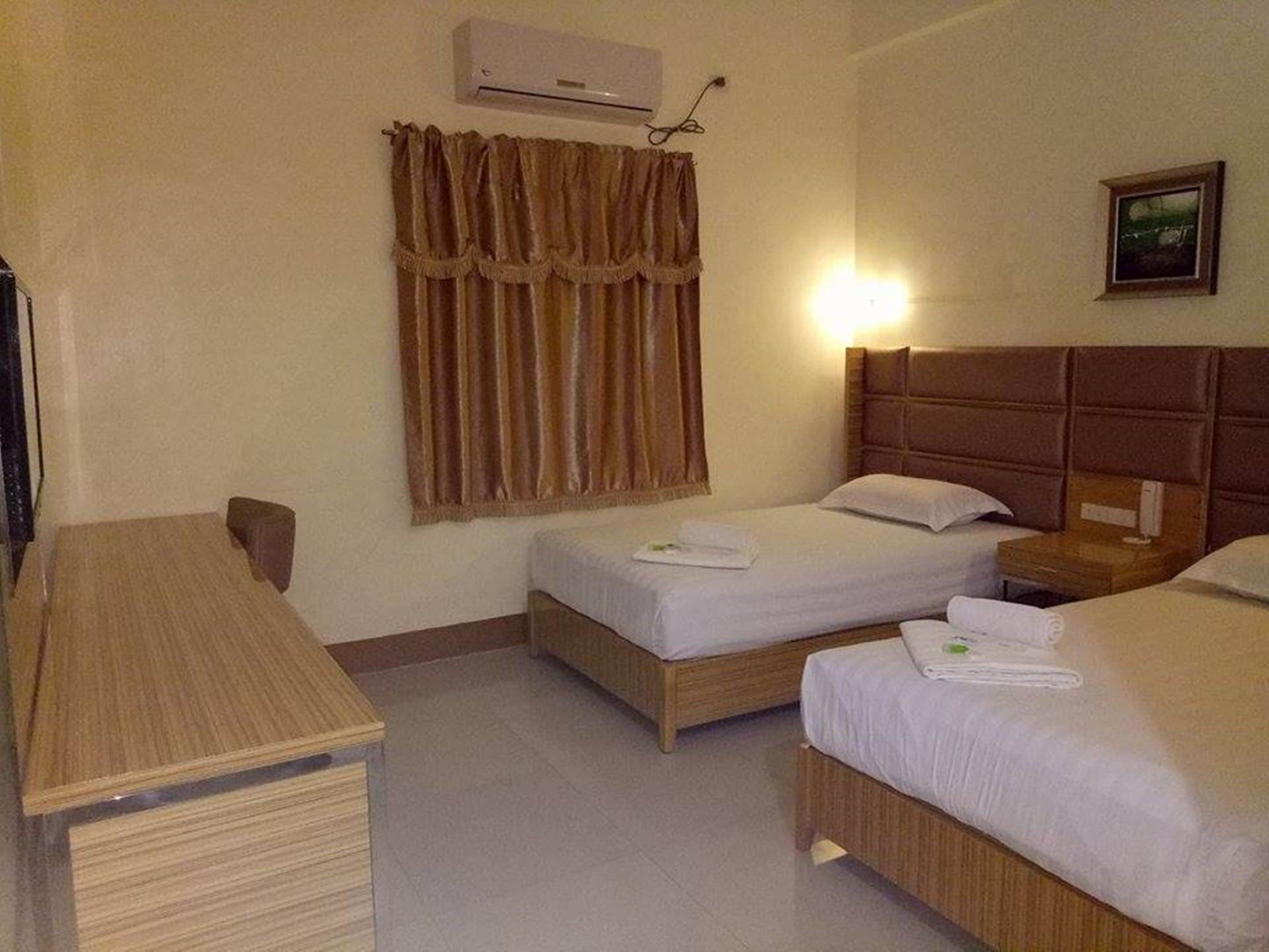 A hotel room with two beds, a wooden desk, a wall-mounted air conditioner, and a framed picture on the wall.
