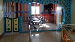 Una habitación con pared a rayas coloridas, un separador de vidrio y una zona de comedor con sillas y mesas.