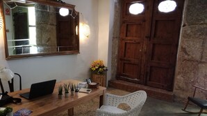 A wooden desk with a laptop, several potted plants, and a mirror. There are wicker chairs and a small table with a vase of flowers. A wooden door with a circular window is visible in the background. - OttoH Charm Stay (Valencia)