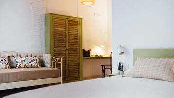 Un dormitorio con una cama, un armario verde, un escritorio con lámpara y una silla.