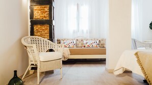 A room with a brick wall, a white wicker chair, a sofa with patterned cushions, and a bed with a beige cover. - OttoH Charm Stay (Valencia)