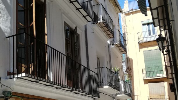 A narrow street with buildings featuring balconies and wooden doors. - OttoH Charm Stay (Valencia)
