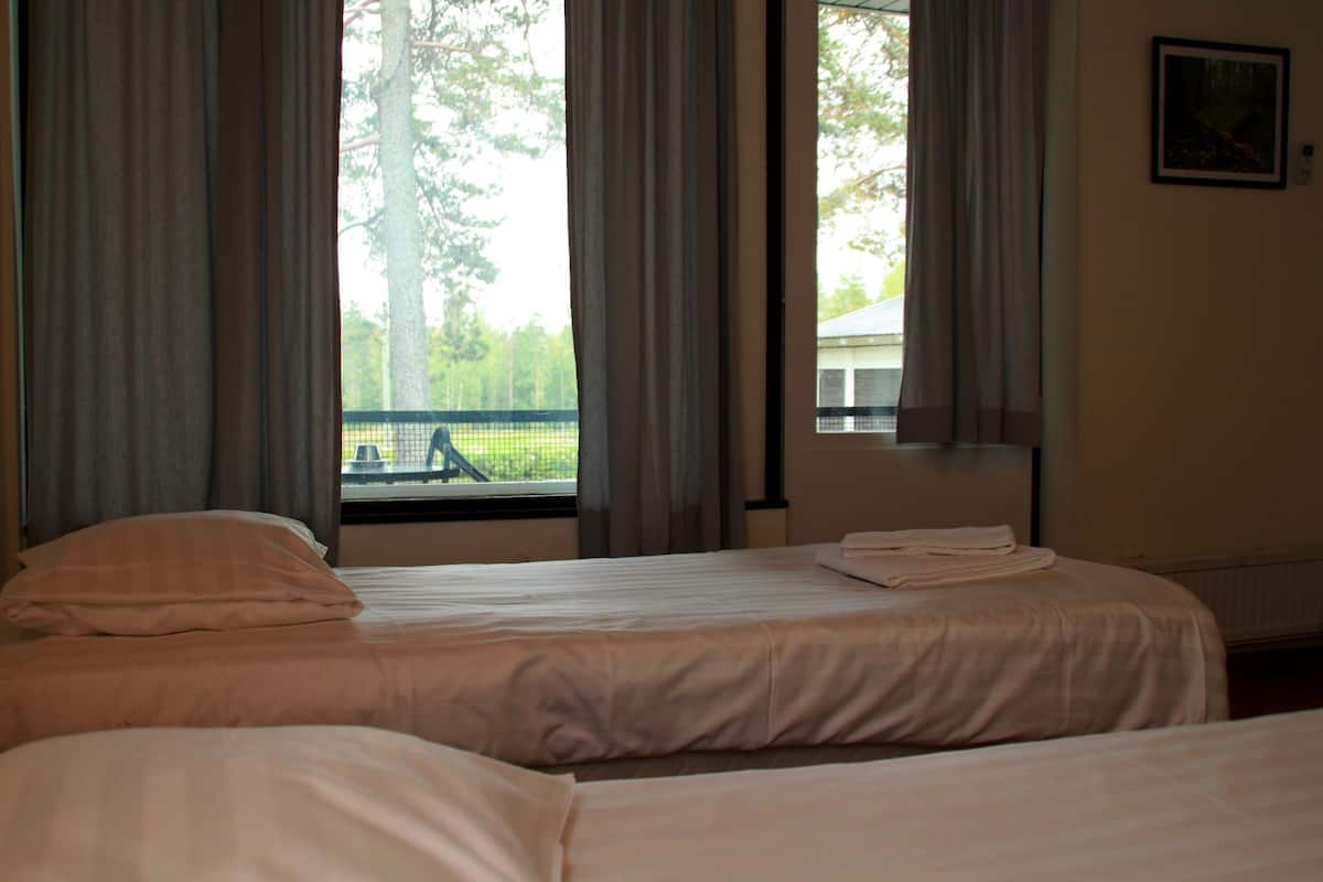 A hotel room with two beds, a window with curtains, and a view of a tennis court.
