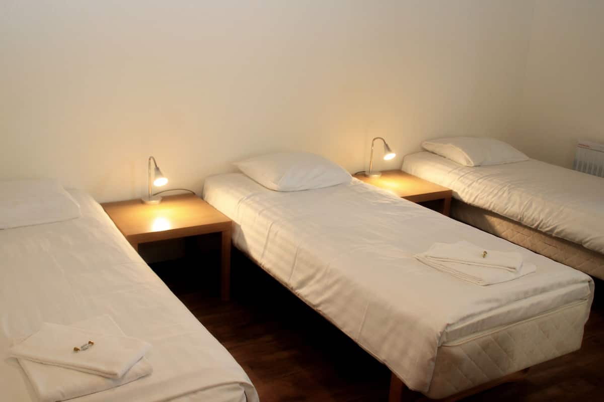 A room with three single beds, each with a bedside table and a lamp.