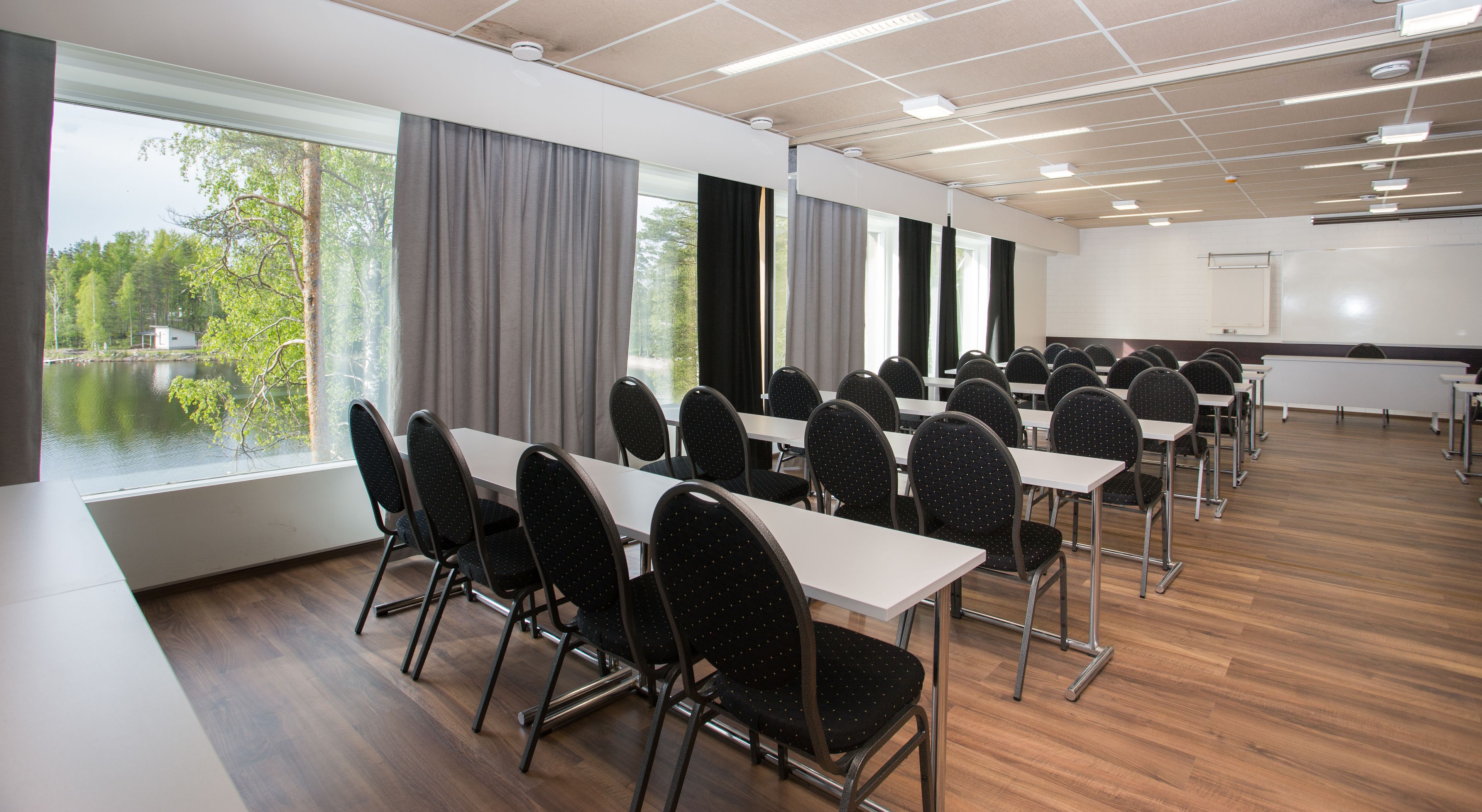 Un salón de conferencias con vistas a un lago, amplias ventanas con cortinas y una pizarra.
