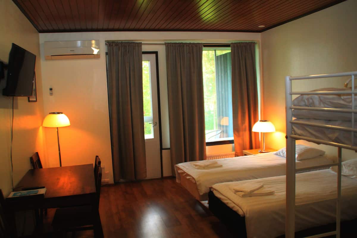 A hotel room with two beds, a TV, a desk, and a window with curtains.