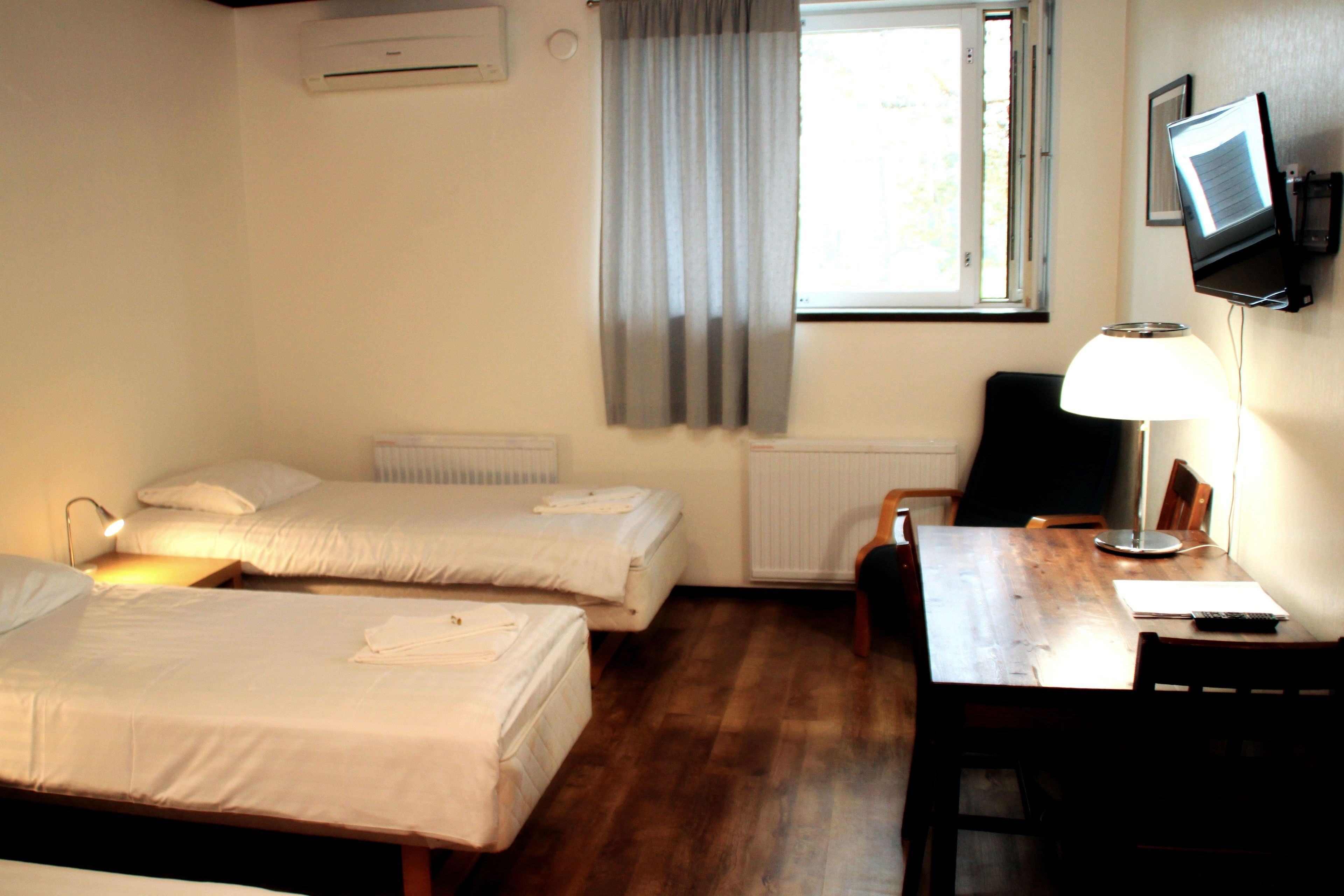 Habitació d'hotel amb dos llits, una escriptori, una cadira, un televisor i una finestra amb cortines.