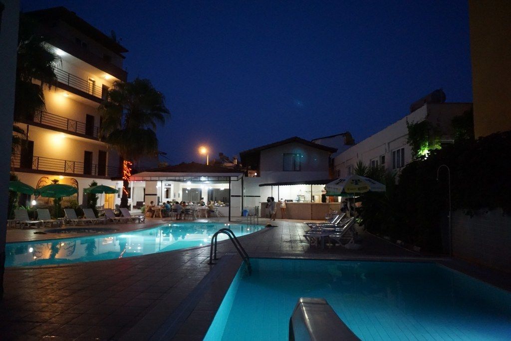 A swimming pool area with lounge chairs and umbrellas, surrounded by buildings with balconies and outdoor seating.