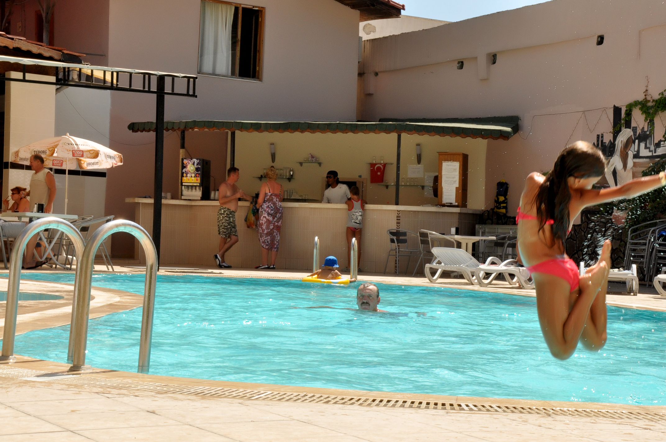 Une piscine entourée de personnes, un bar et des chaises longues.