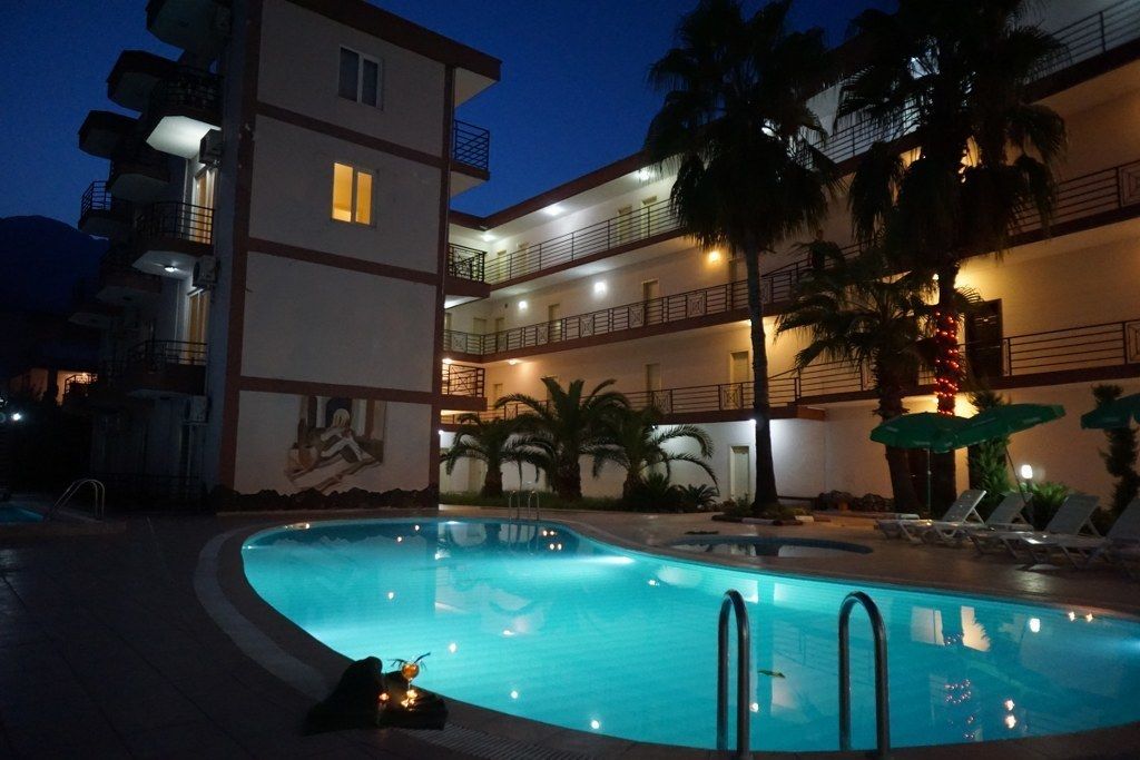 A multi-story hotel with a swimming pool, palm trees, and outdoor seating.