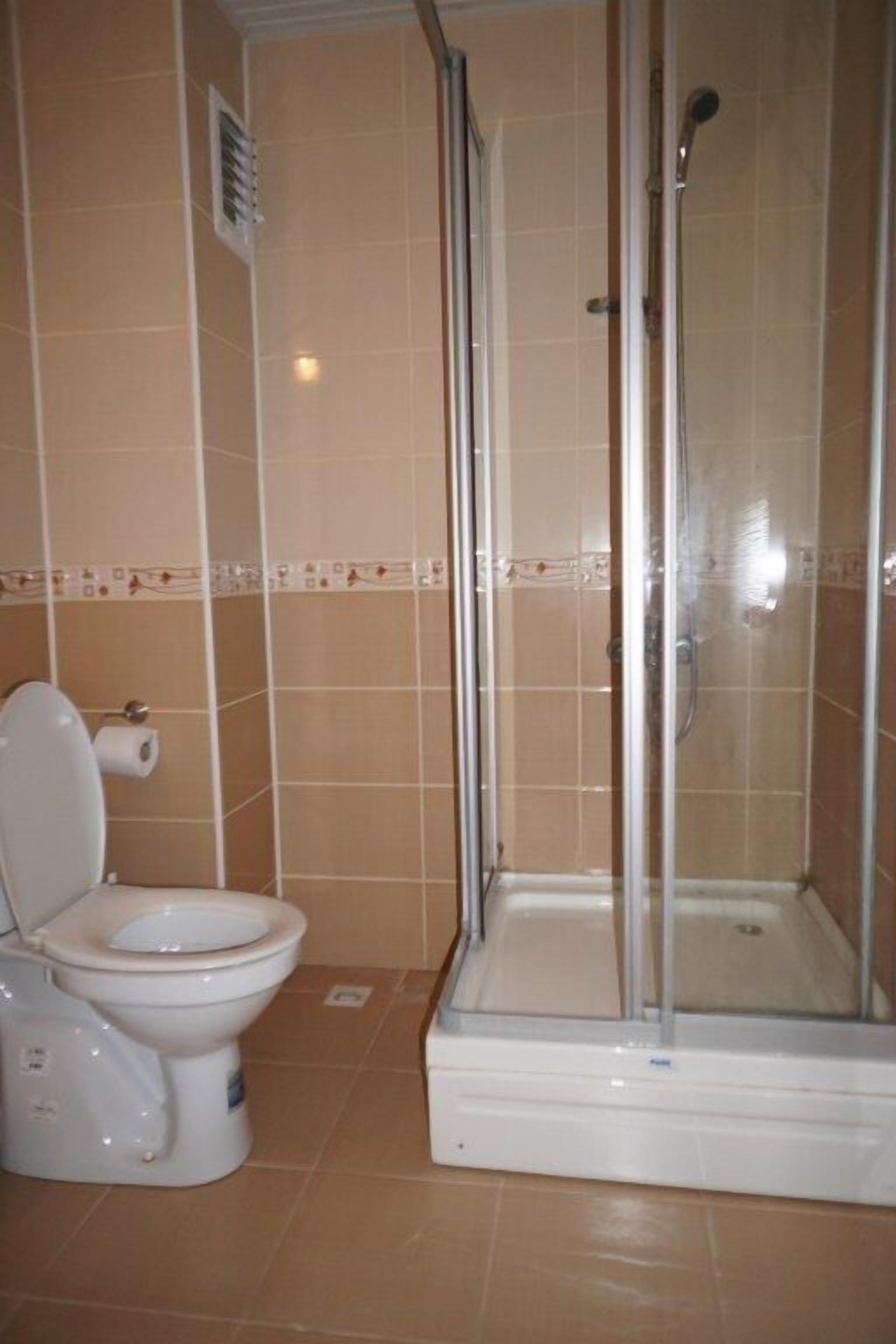 A bathroom with a toilet, shower, and tiled walls.