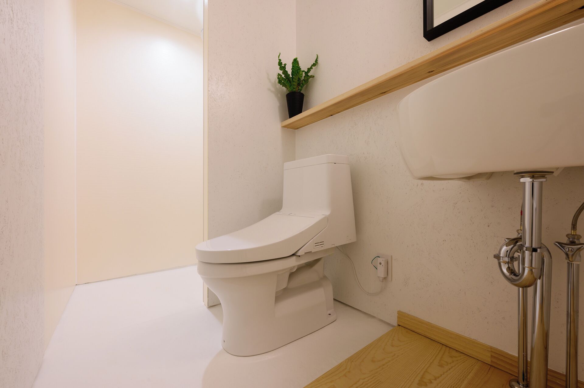 Une salle de bain moderne avec des toilettes blanches, un plancher en bois et une petite plante en pot posée sur une étagère.
