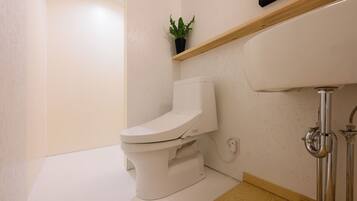Une salle de bain moderne avec des toilettes blanches, un plancher en bois et une petite plante en pot posée sur une étagère.