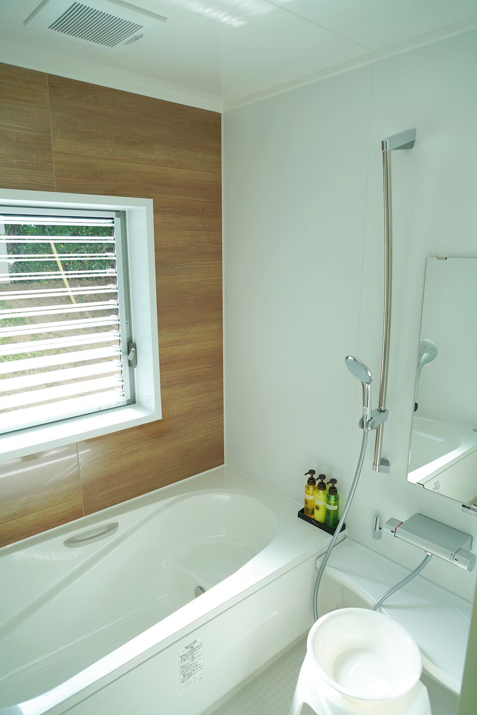 A modern bathroom with a bathtub, a shower, a window with blinds, and a mirror.