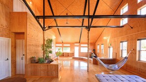 Ruime kamer met houten wanden en vloeren, een hangmat, een comfortabele zitting en een groot raam dat voor natuurlijk licht zorgt.