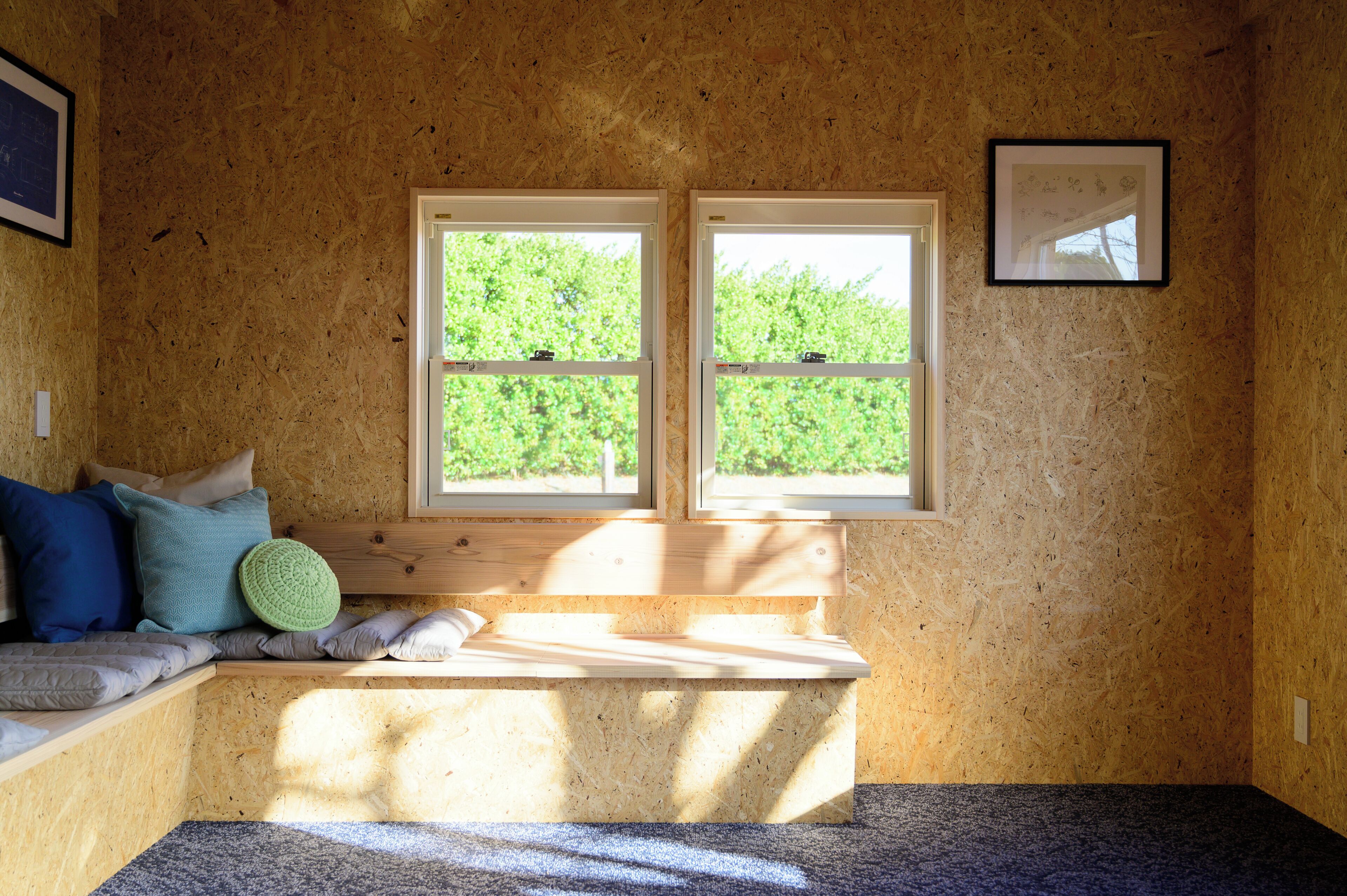 A room with a wooden bench, two windows, and a framed picture on the wall.