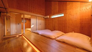 Een kamer met houten wanden en vloeren, twee bedden met witte lakens, een raam en een deur naar een andere kamer.